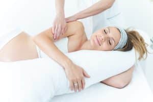 Pregnant woman lying on her side, receiving a body massage.